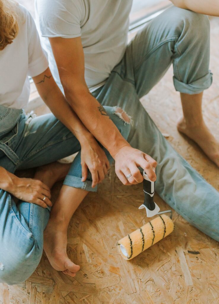 man and woman sitting on the floor with a paint roller